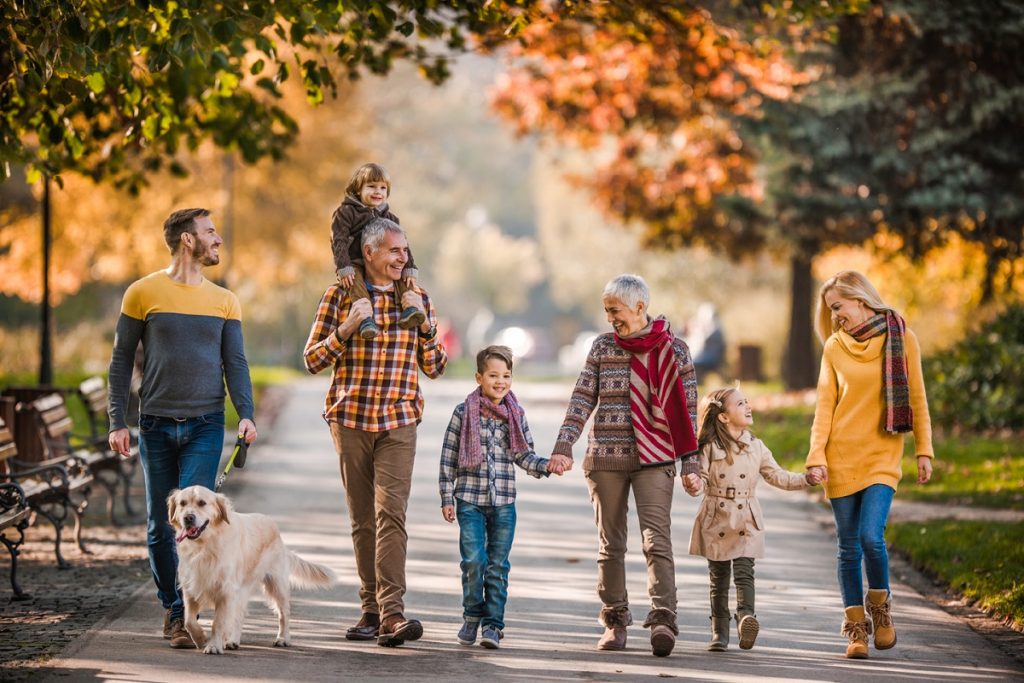 Familie extinsă fericită care își plimbă câinele și comunică într-o zi de toamnă în parc.