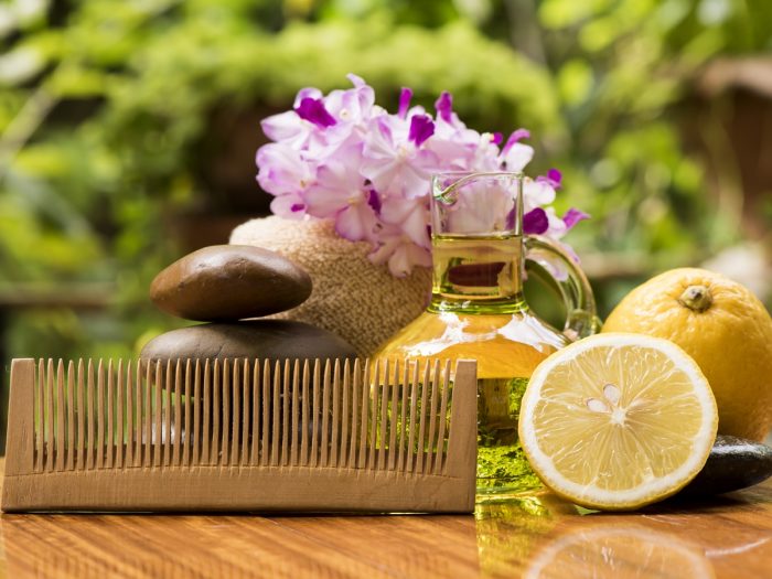Ulei esențial păstrat într-un borcan de sticlă, alături de flori de lavandă, portocale și un pieptene, deasupra unei mese de lemn.