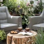 Un colț de relaxare pe o terasă însorită, cu două fotolii confortabile și o măsuță de lemn natural. Pe măsuță sunt două cești de cafea aburinde, alături de o carte deschisă și câteva biscuiți artizanali. Fundalul arată plante verzi și flori, sugerând o atmosferă organică și naturală, în armonie cu caracterul bio al cafelei.