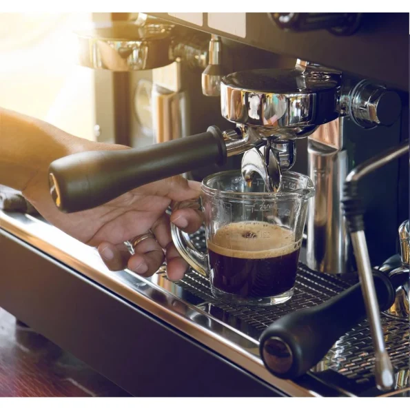un espressor manual într-o cafenea artizanală. Lumina blândă evidențiază jetul de cafea proaspătă care curge în ceașca