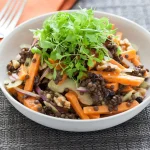 O salată sănătoasă și colorată cu linte neagră Beluga, morcovi proaspeți, ceapă roșie, nuci și microplante verzi, servită într-un bol alb elegant.