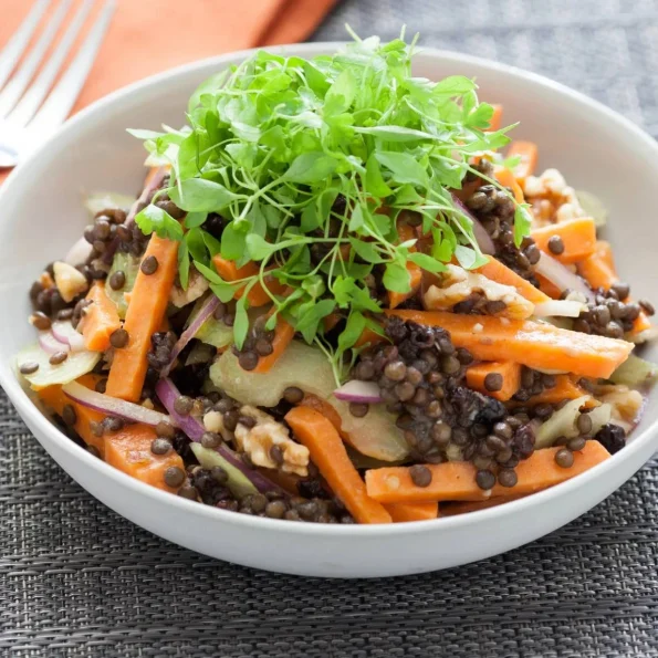 O salată sănătoasă și colorată cu linte neagră Beluga, morcovi proaspeți, ceapă roșie, nuci și microplante verzi, servită într-un bol alb elegant.
