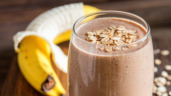 5 Remedii Care Te Ajută Să Reduci Oboseala Musculară Smoothie cremos cu banane și cacao, decorat cu fulgi de ovăz, servit într-un pahar înalt pe o masă de lemn rustică.